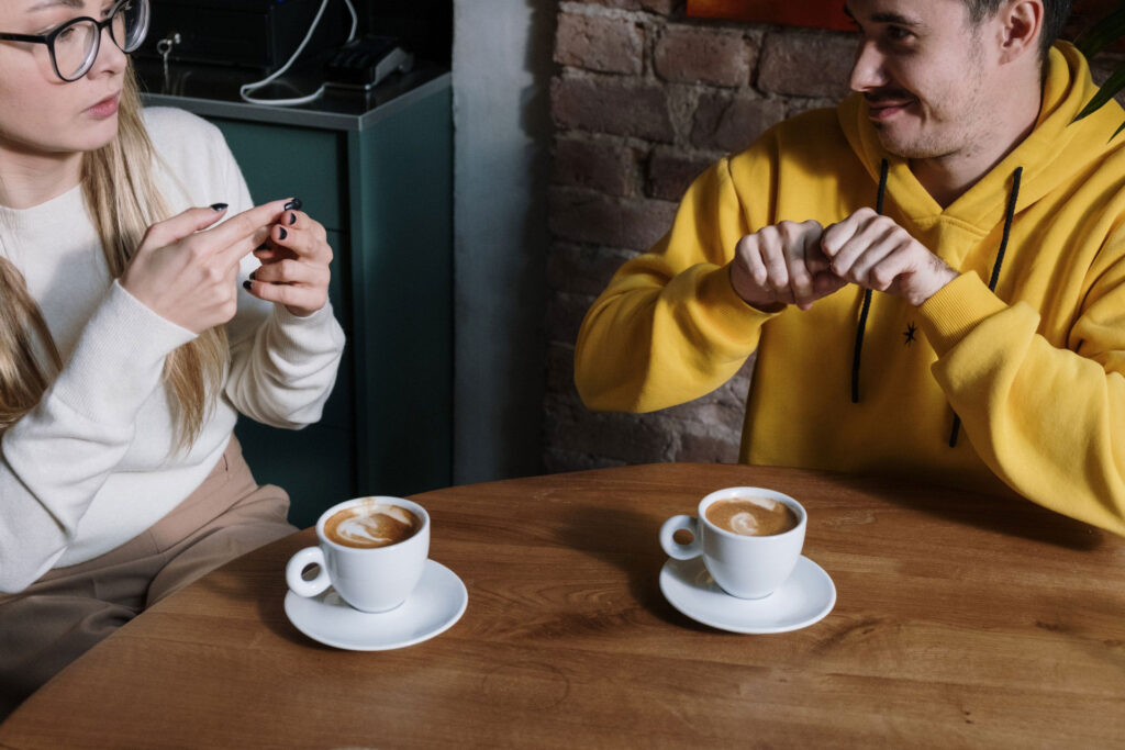 Two people sitting at a table with a coffee in front of them speaking in sign language